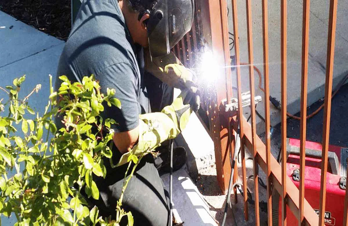 A technician welding a metal gate under bright sunlight, showcasing reliable gate repair services in Houston.