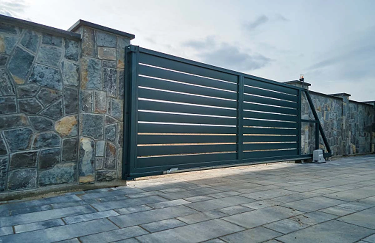 Black aluminum sliding gate installed between stone columns, showing design flaws and lack of drainage as key reasons gates fail in Houston.